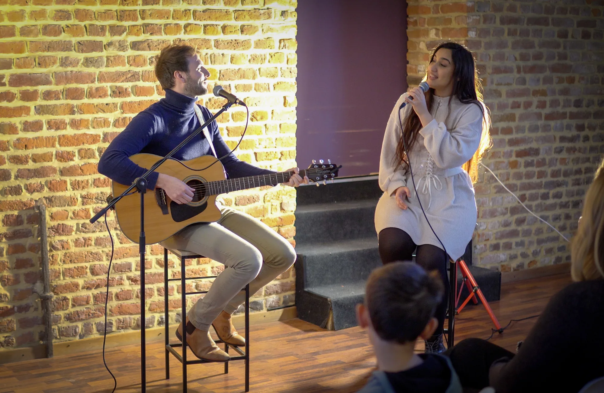 Un concert dans le lieu : un guitariste et une chanteuse devant un public assis.