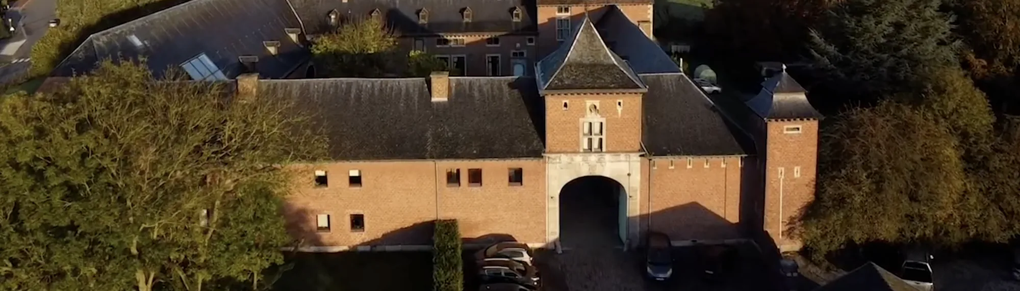Vue aérienne de l'ancienne ferme : le porche voûté, la cour pavée et les longues ailes de briques.
